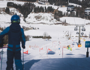 Ein Skifahrer blickt auf die Funslope hinunter, während die Steinbergbahn Kabinen über die verschneite Berglandschaft schweben. | © Stefanie Oberhauser